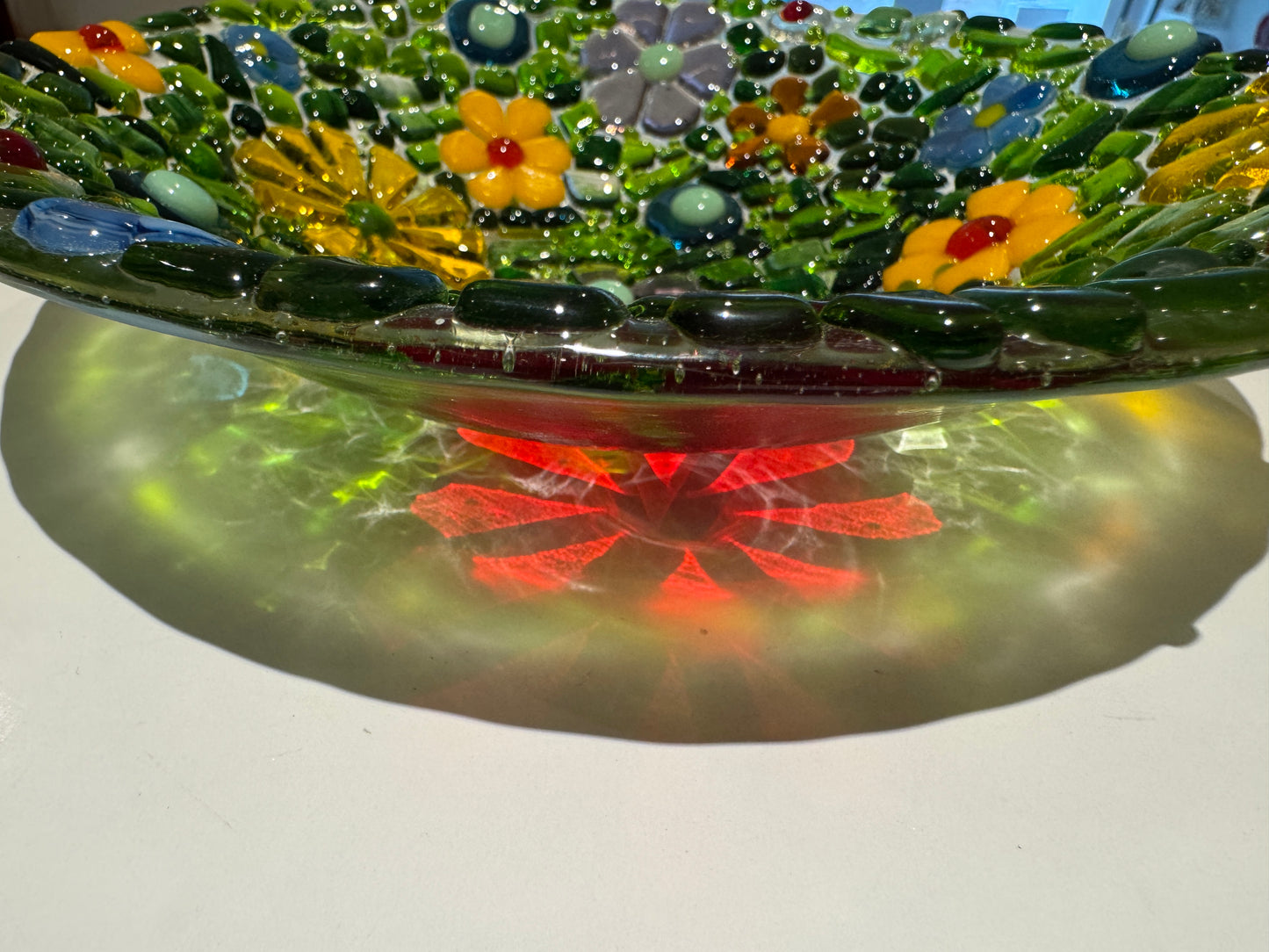 Decorative glass bowl with colorful flowers and green base on a white background